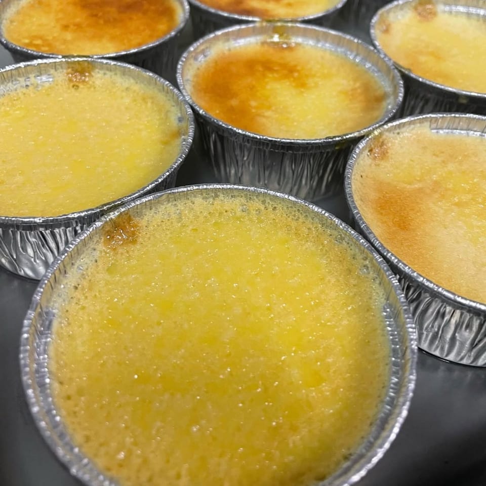 Several small, round creme brulees in foil cups, some with lightly browned tops.